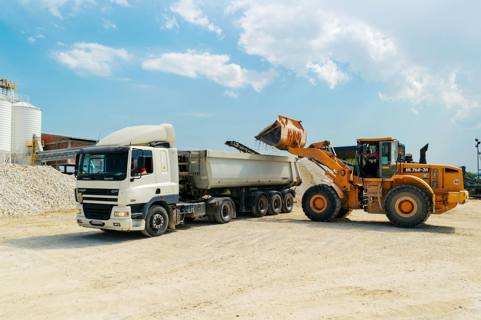 Gelber Radlader belädt einen weißen LKW mit Schüttgut auf einer Baustelle.